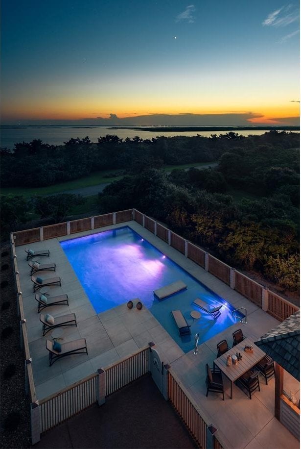 view of pool with a water view, a jacuzzi, fence, and a patio