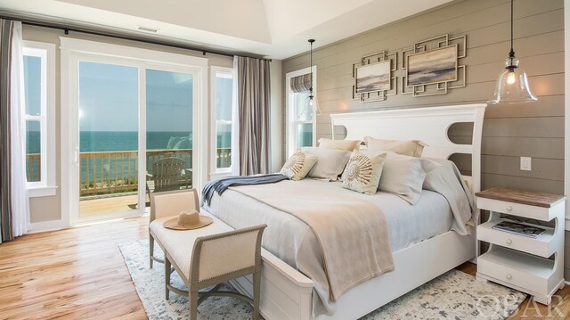 bedroom with light wood-style floors, access to outside, a water view, and wood walls