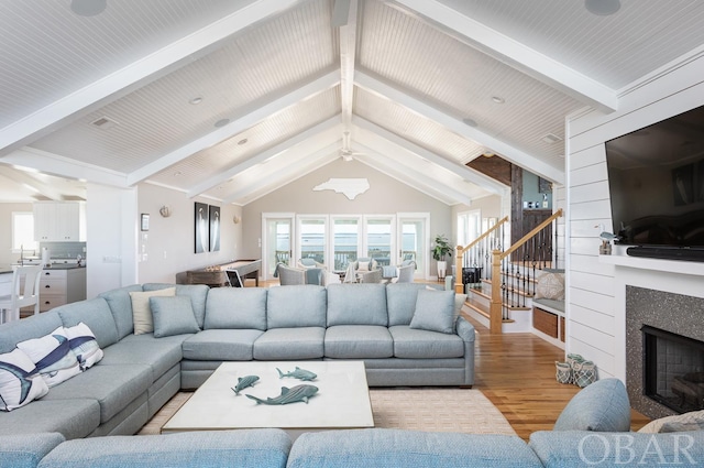 living area featuring lofted ceiling with beams, light wood finished floors, a fireplace, and stairway