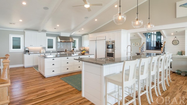 kitchen featuring stainless steel double oven, a spacious island, paneled built in fridge, white cabinetry, and hanging light fixtures