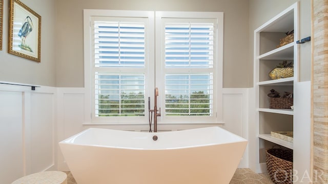 full bath with built in shelves, a freestanding tub, a wainscoted wall, and a decorative wall