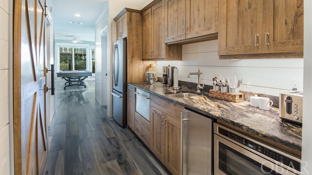 kitchen featuring brown cabinets, a warming drawer, freestanding refrigerator, a sink, and dark stone countertops