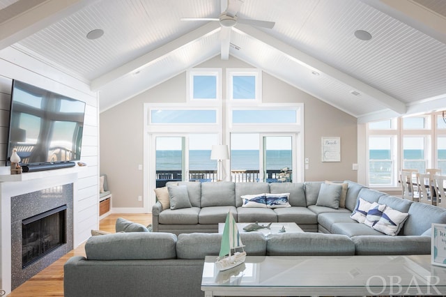 living room featuring beamed ceiling, a water view, light wood-type flooring, a fireplace, and high vaulted ceiling