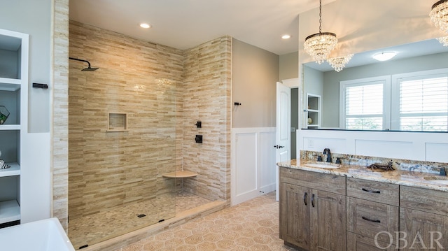 full bathroom with a wainscoted wall, a sink, tiled shower, double vanity, and an inviting chandelier