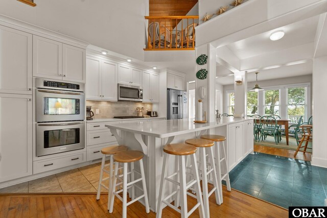 1148 Dunton Dr Lot 337, Corolla, NC 27927 - kitchen with decorative backsplash, a kitchen breakfast bar, light wood-type flooring, light countertops, and stainless steel appliances