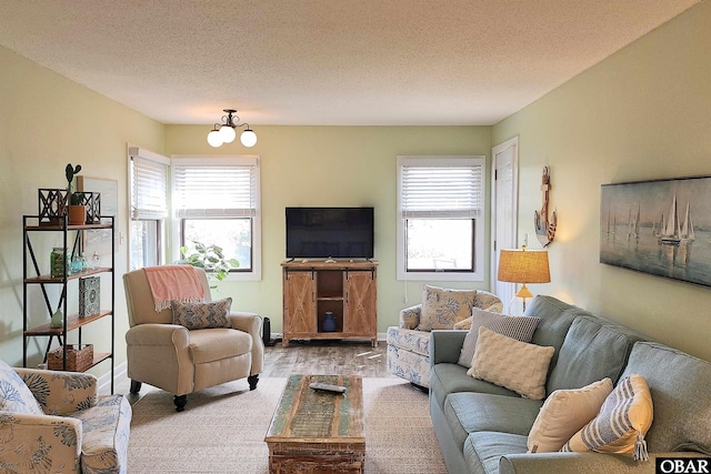 living room featuring a chandelier, a textured ceiling, baseboards, and wood finished floors