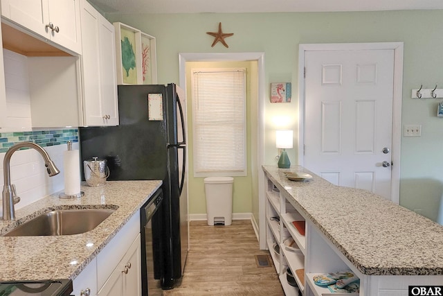 kitchen with black dishwasher, a sink, white cabinetry, and decorative backsplash