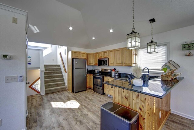 kitchen featuring lofted ceiling, hanging light fixtures, appliances with stainless steel finishes, light wood-style floors, and a peninsula