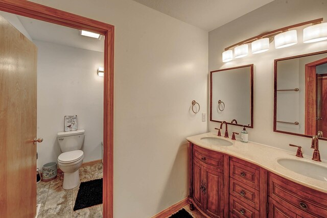 bathroom featuring baseboards, a sink, toilet, and double vanity