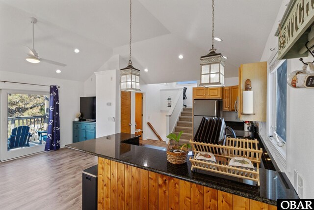 kitchen with dark stone counters, lofted ceiling, wood finished floors, refrigerator, and a peninsula