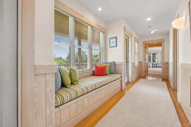 hall with light wood-style floors, recessed lighting, a healthy amount of sunlight, and a wainscoted wall