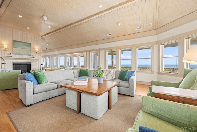 living area with wooden ceiling, light wood-style flooring, a fireplace, a water view, and visible vents