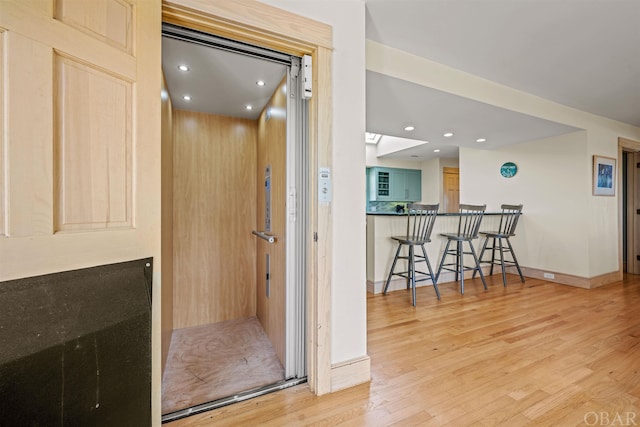 interior space with a skylight, baseboards, elevator, light wood-style flooring, and recessed lighting