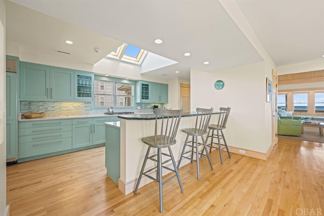 kitchen featuring a skylight, light wood-style flooring, glass insert cabinets, a kitchen bar, and green cabinetry