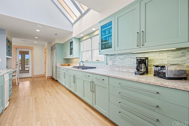 kitchen with tasteful backsplash, glass insert cabinets, green cabinets, and light wood-style flooring