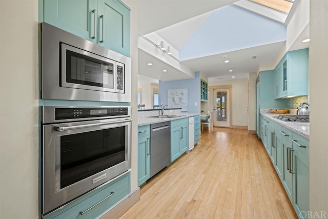 kitchen with light stone counters, light wood-style flooring, a sink, appliances with stainless steel finishes, and tasteful backsplash