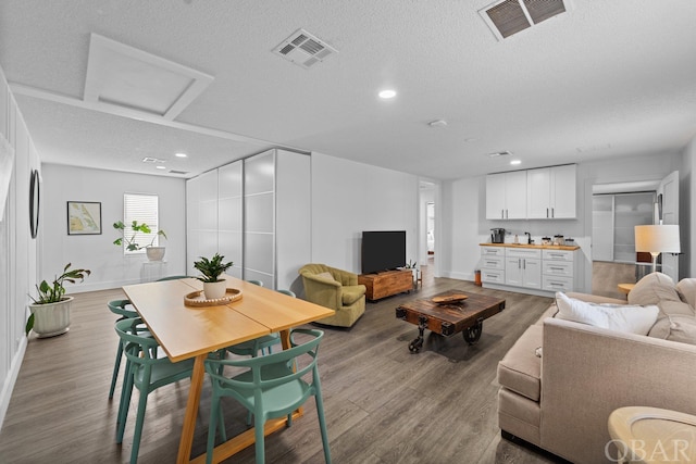 living room with attic access, visible vents, light wood-style flooring, and a textured ceiling