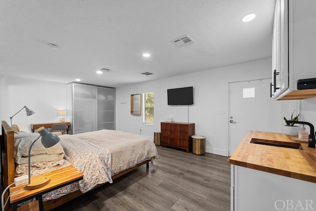 bedroom featuring a sink, a textured ceiling, wood finished floors, and visible vents