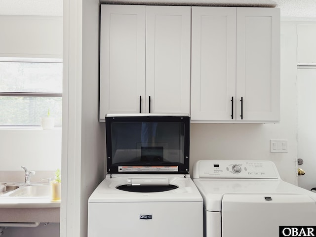 clothes washing area featuring a sink, a textured ceiling, washing machine and clothes dryer, and cabinet space