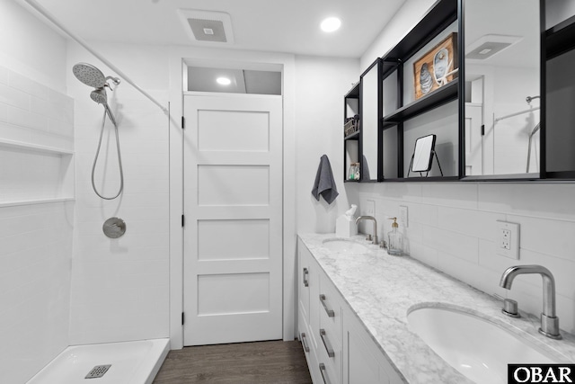 full bathroom featuring wood finished floors, tiled shower, a sink, and decorative backsplash