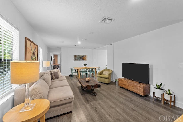 living area with a textured ceiling, visible vents, and wood finished floors