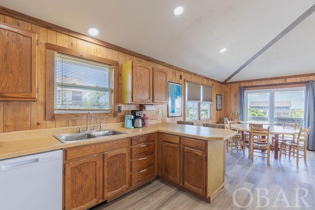 kitchen with a peninsula, white dishwasher, light countertops, wood walls, and a sink