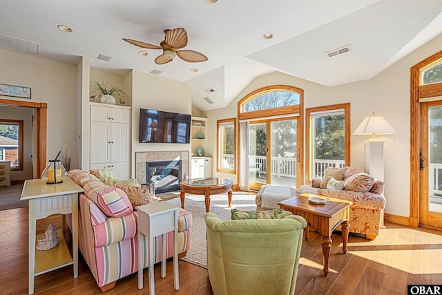 living room with a fireplace, visible vents, vaulted ceiling, and wood finished floors