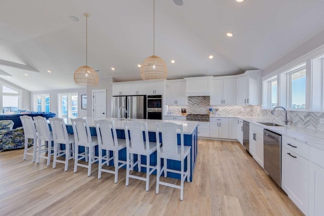 kitchen featuring stainless steel appliances, white cabinetry, open floor plan, hanging light fixtures, and an island with sink