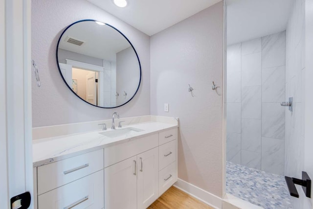 bathroom with wood finished floors, vanity, visible vents, baseboards, and a tile shower