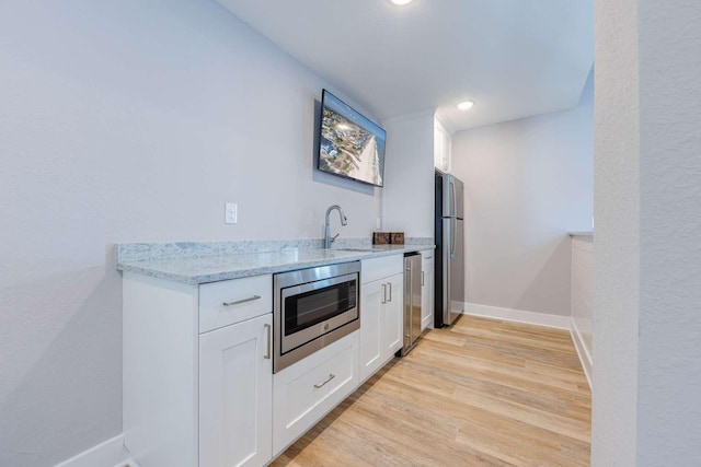 kitchen featuring white cabinets, appliances with stainless steel finishes, light stone counters, light wood-type flooring, and a sink