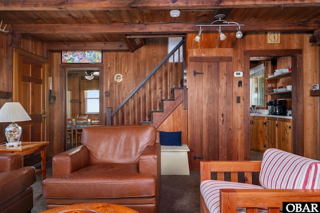 living room featuring wooden ceiling, beamed ceiling, carpet, stairs, and wood walls