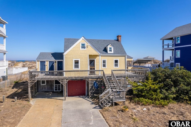 view of front facade featuring a chimney, a shingled roof, concrete driveway, stairway, and an attached garage