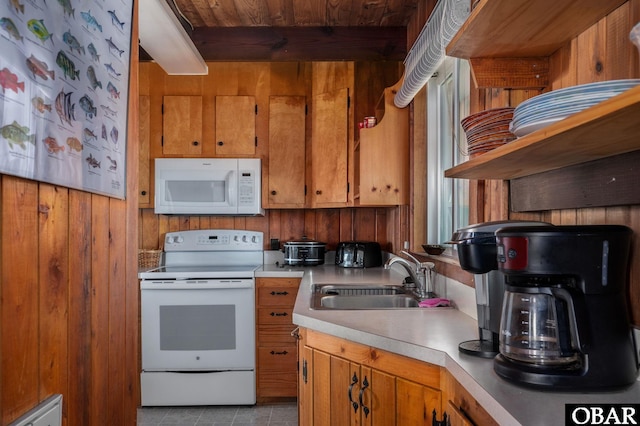 kitchen featuring white appliances, wooden walls, brown cabinetry, light countertops, and a sink