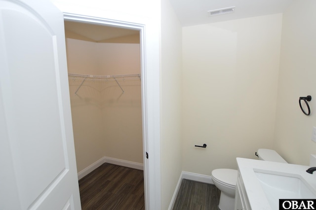 bathroom with a walk in closet, visible vents, toilet, wood finished floors, and baseboards