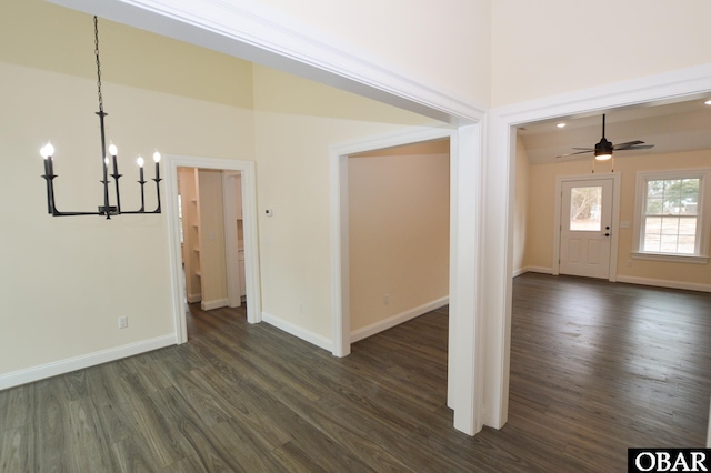 interior space with baseboards, dark wood-type flooring, and ceiling fan with notable chandelier