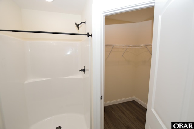 bathroom with a stall shower, a walk in closet, baseboards, and wood finished floors