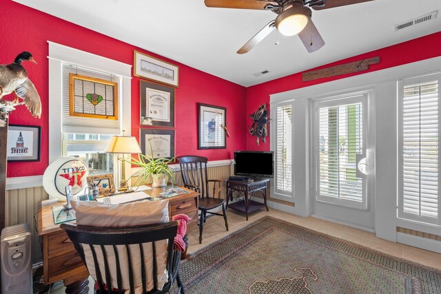 tiled home office featuring a wainscoted wall, visible vents, and a ceiling fan