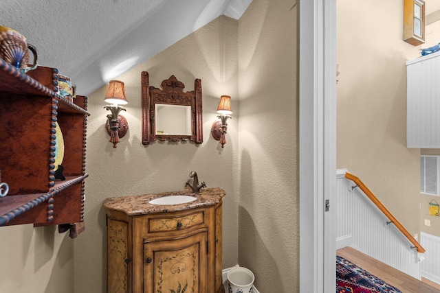 bathroom featuring visible vents, wainscoting, vanity, a textured ceiling, and wood finished floors