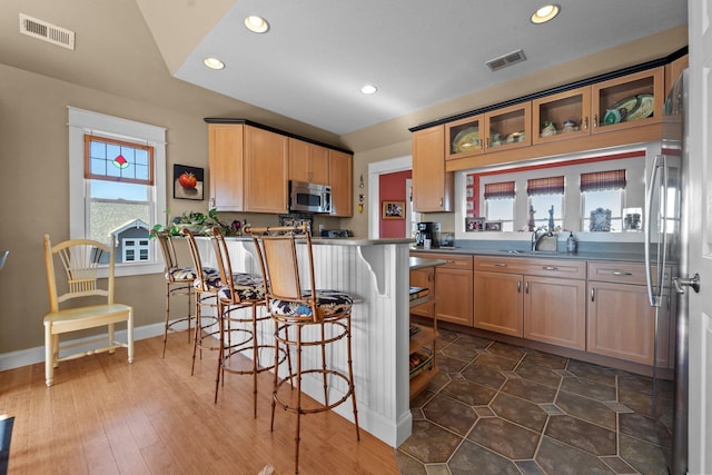 kitchen with dark countertops, visible vents, appliances with stainless steel finishes, glass insert cabinets, and a peninsula