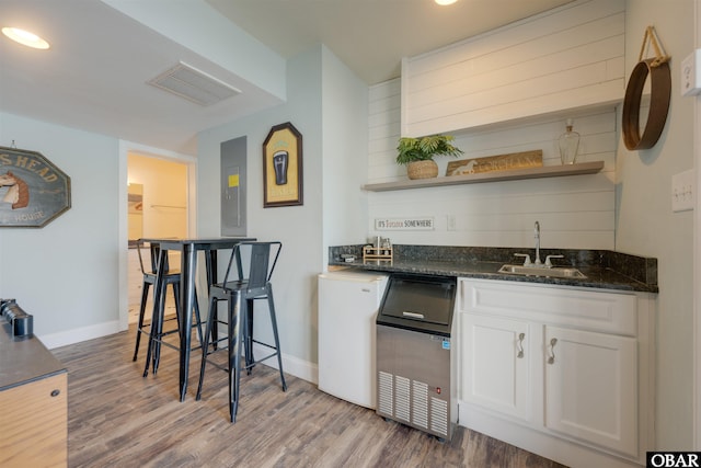 bar with indoor wet bar, visible vents, wood finished floors, a sink, and baseboards