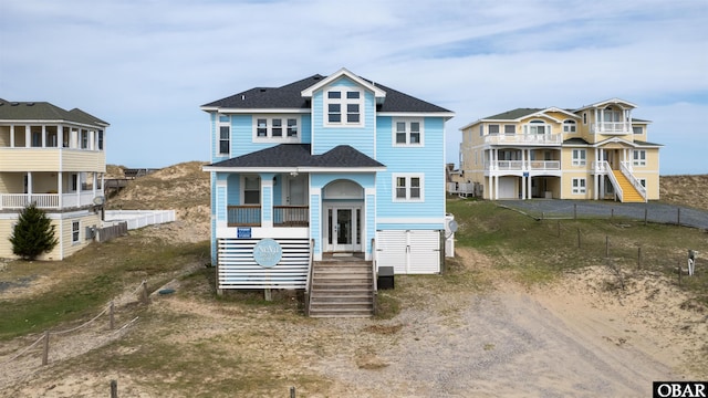 raised beach house featuring a shingled roof and stairway