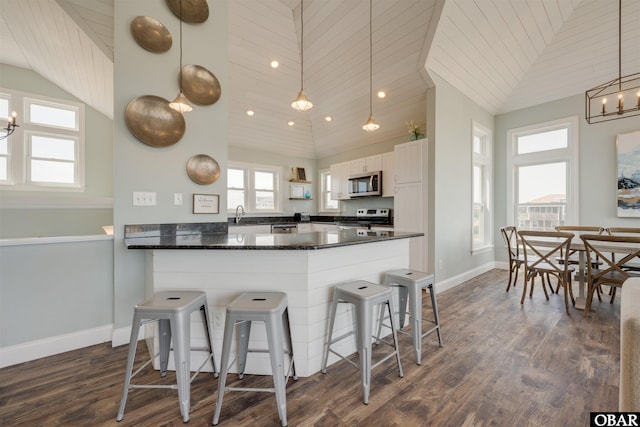 kitchen with a kitchen bar, a peninsula, vaulted ceiling, appliances with stainless steel finishes, and baseboards
