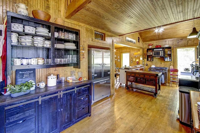 kitchen with built in appliances, wooden walls, wooden ceiling, and wood finished floors