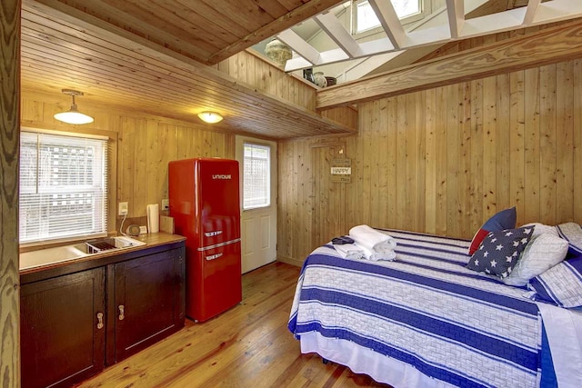 bedroom with a skylight, light wood-type flooring, wood walls, and freestanding refrigerator