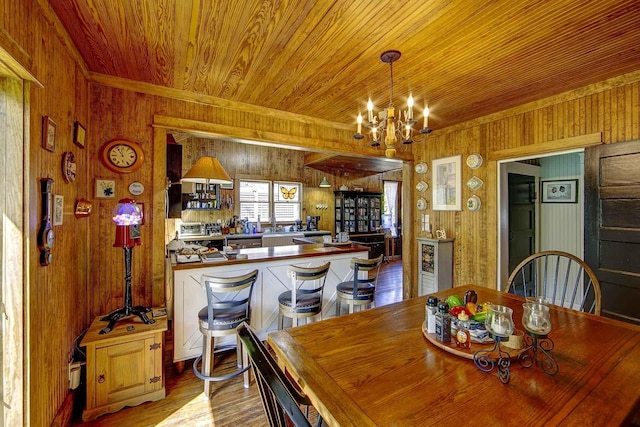 dining room with ornamental molding, wood finished floors, wooden walls, a chandelier, and wooden ceiling