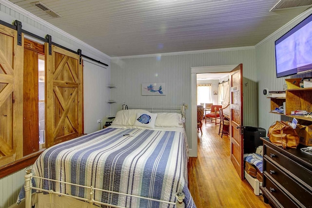 bedroom featuring ornamental molding, visible vents, a barn door, and wood finished floors