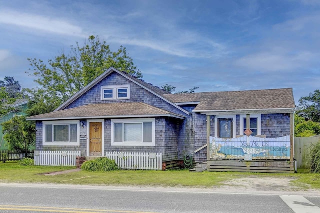 view of front of home with covered porch, a fenced front yard, and roof with shingles