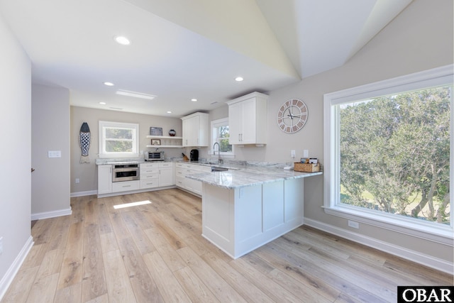 kitchen with light stone counters, a peninsula, stainless steel oven, white cabinets, and open shelves