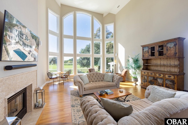 living area featuring light wood-style flooring, a high ceiling, baseboards, and a tile fireplace