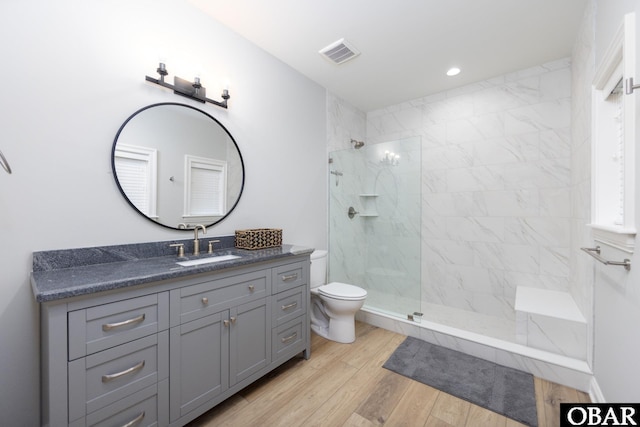 bathroom featuring wood finished floors, visible vents, toilet, vanity, and a walk in shower